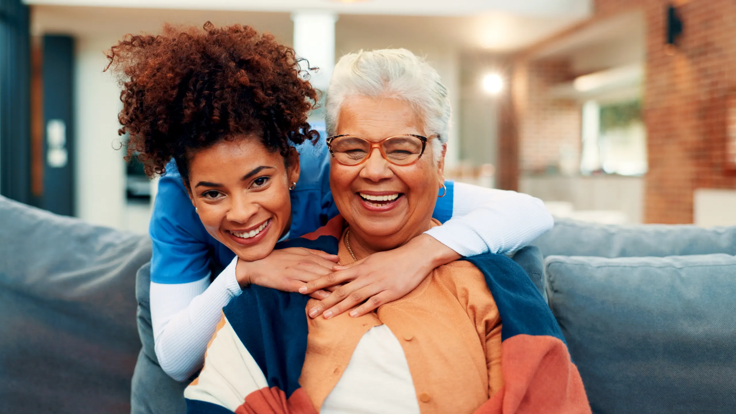 A nurse and an older woman sharing a hug on a sofa