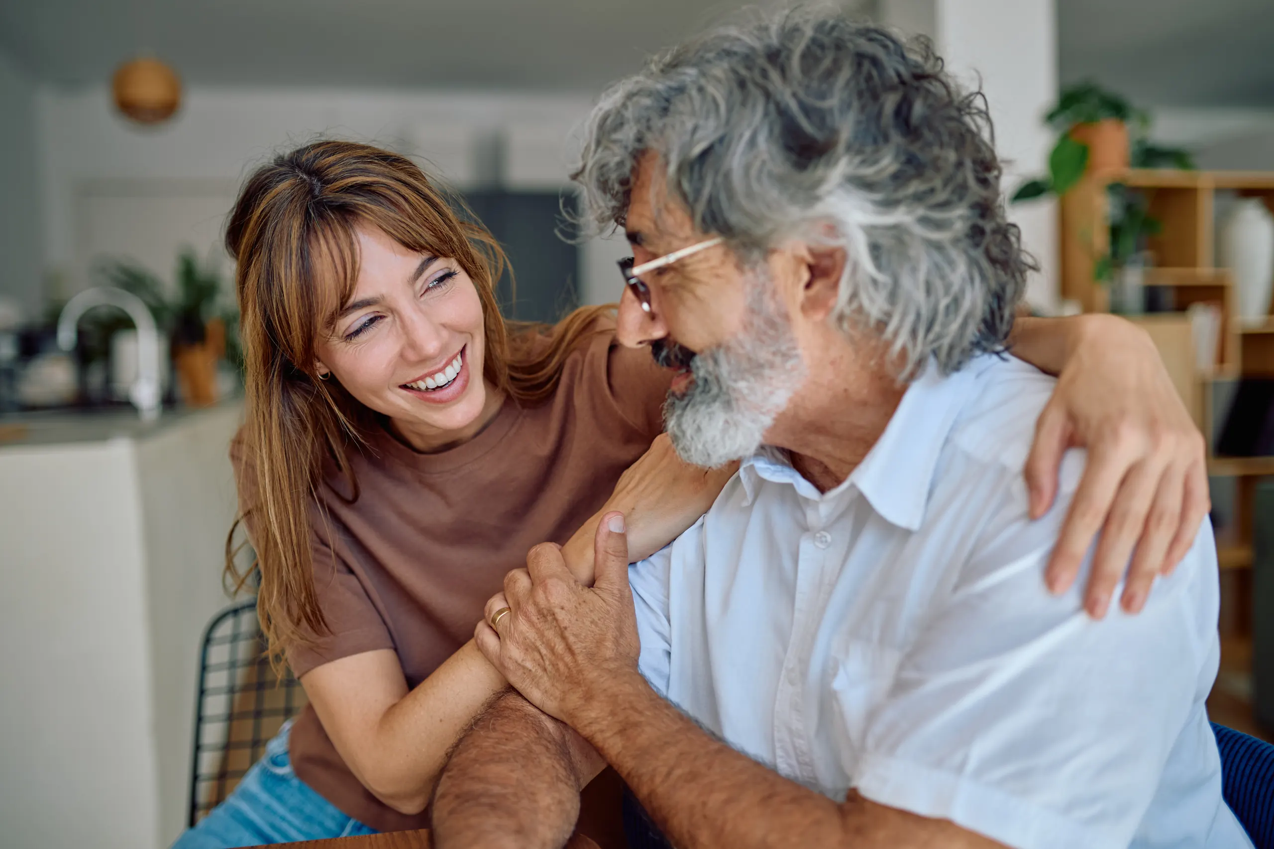 An adult daughter hugging her senior father at home