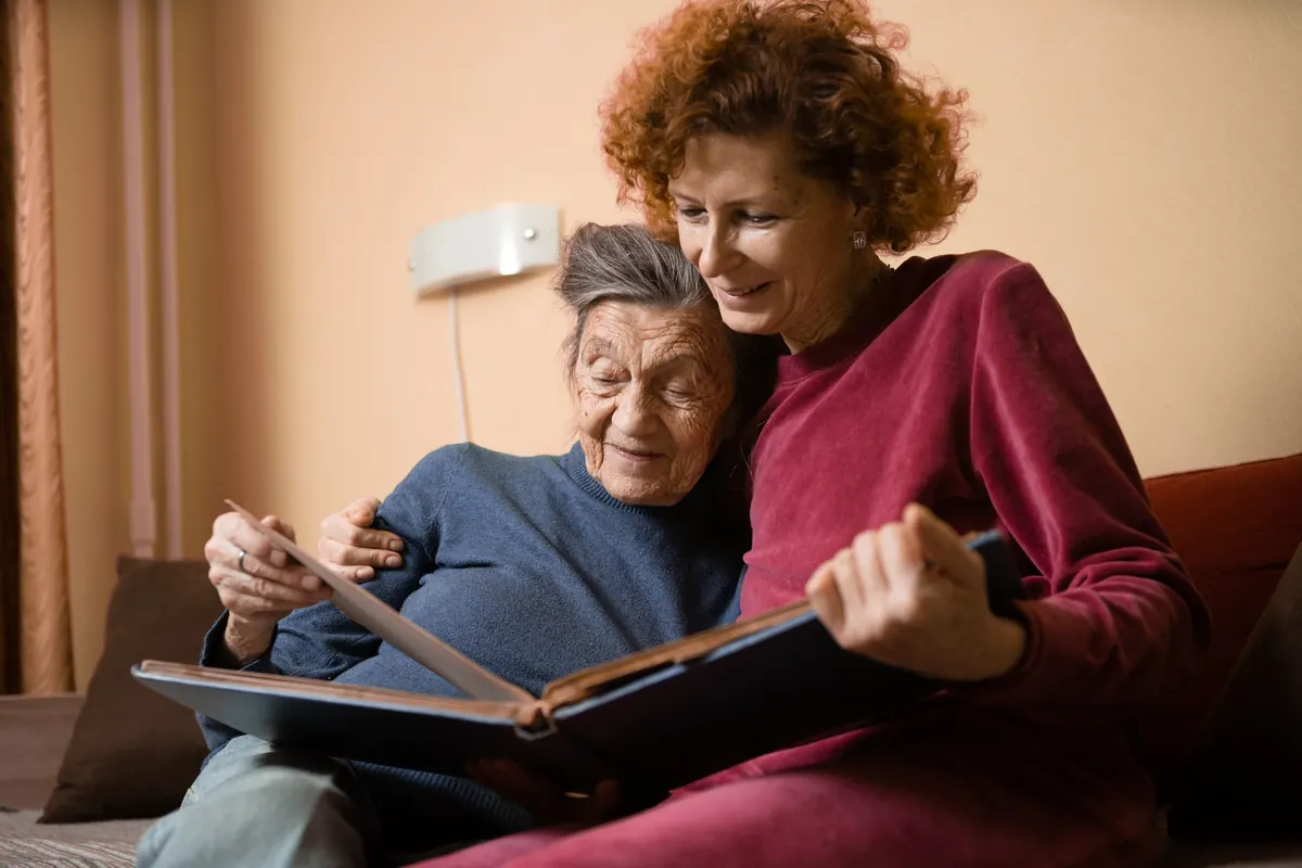 A senior woman and her adult daughter looking through a photo album