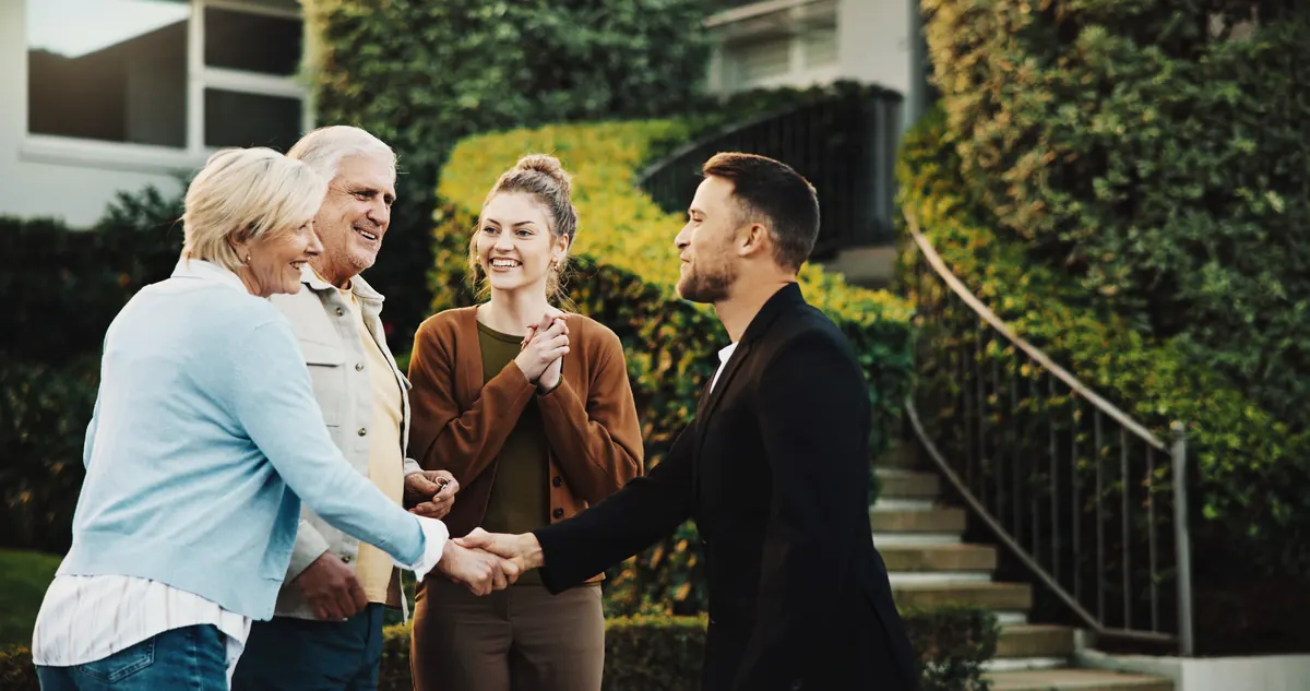 An elderly couple greeting a visitor with a handshake